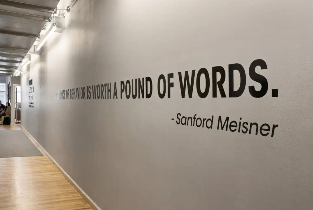 Sanford Meisner's quote 22 An ounce of behavior is worth a pound of words 22 printed on a blank wall